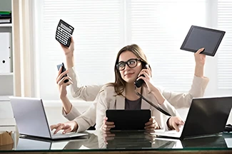 A woman sits at her desk with a laptop and phone, showcasing multitasking skills.